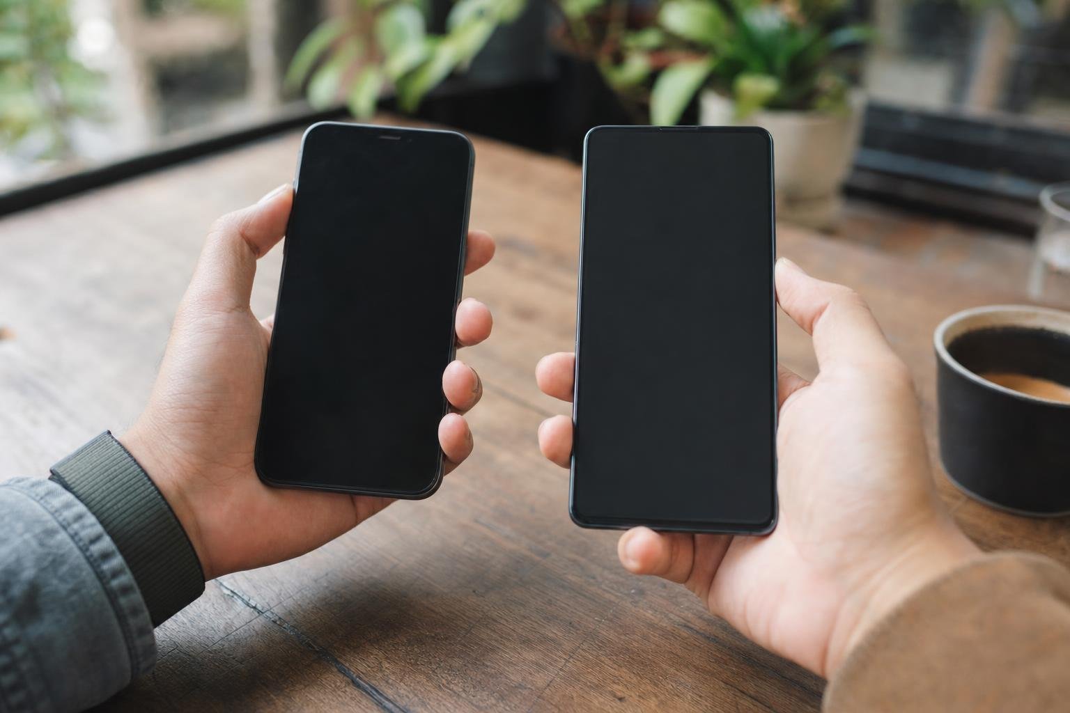 Illustration: two hands, each holding a different smartphone, side by side above a wooden table.