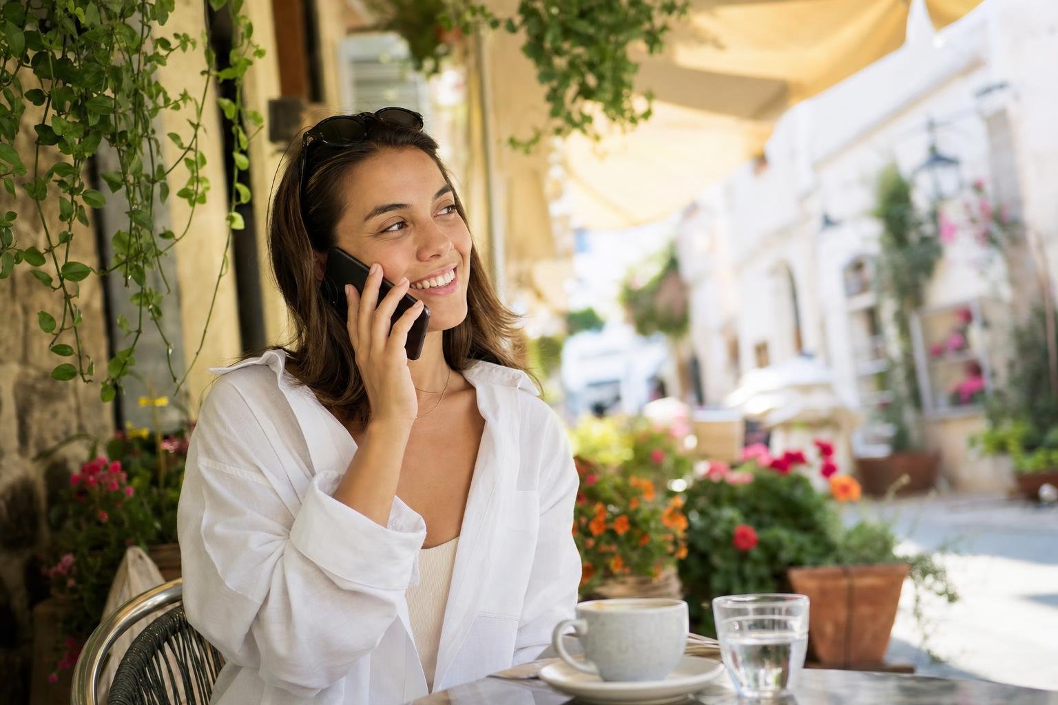 Illustration: a smiling traveller at an outdoor café holding a phone to her ear.